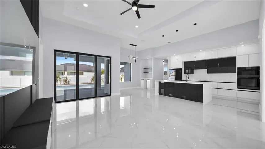 Unfurnished living room featuring light marble finish flooring, ceiling fan, a high ceiling, recessed lighting, and a raised ceiling
