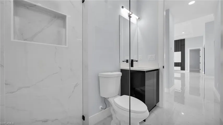 Bathroom featuring vanity, light marble finish floors, recessed lighting, and a marble finish shower