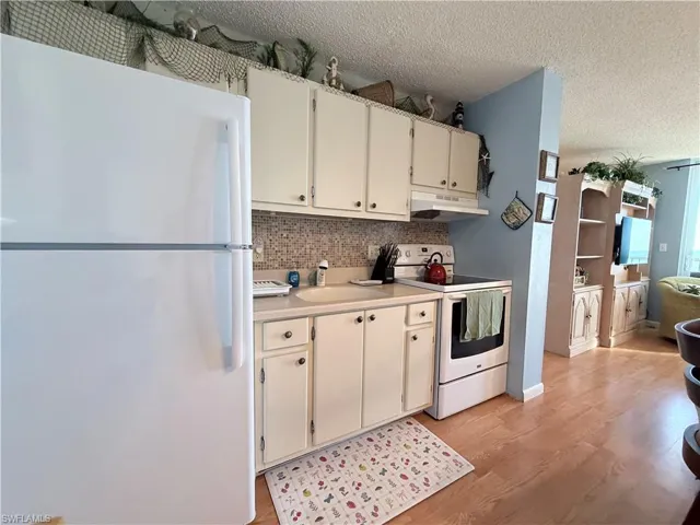 Kitchen featuring white appliances, light countertops, a textured ceiling, under cabinet range hood, and light wood-style flooring