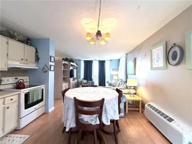 Kitchen featuring white electric range, light countertops, a textured ceiling, a wall mounted air conditioner, and under cabinet range hood