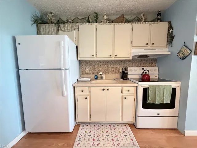Kitchen featuring white appliances, light countertops, decorative backsplash, under cabinet range hood, and light wood finished floors