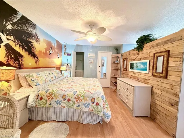 Bedroom featuring wood walls, a textured ceiling, light wood finished floors, and ceiling fan