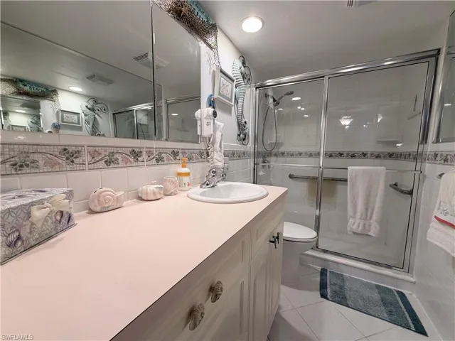 Bathroom featuring vanity, a shower stall, tile walls, light tile patterned floors, and backsplash