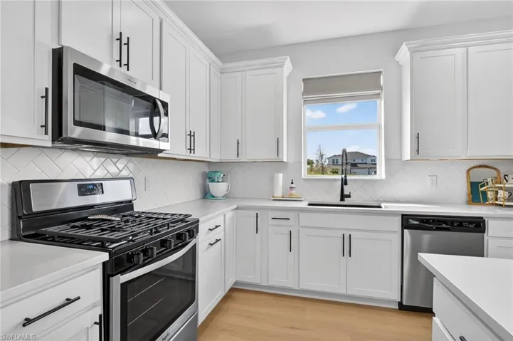 Kitchen featuring stainless steel appliances, white cabinetry and backsplash