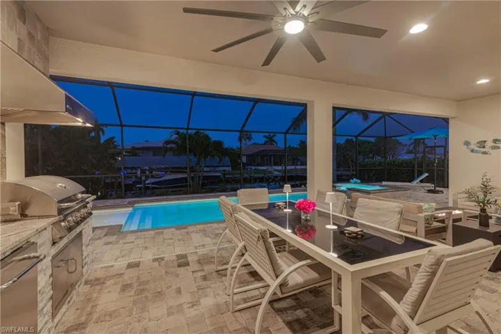 View of pool featuring a patio area, glass enclosure, a ceiling fan, and outdoor dining area