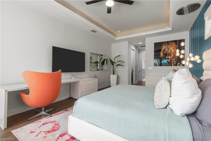 Bedroom with wood finished floors, a tray ceiling, baseboards, and a ceiling fan