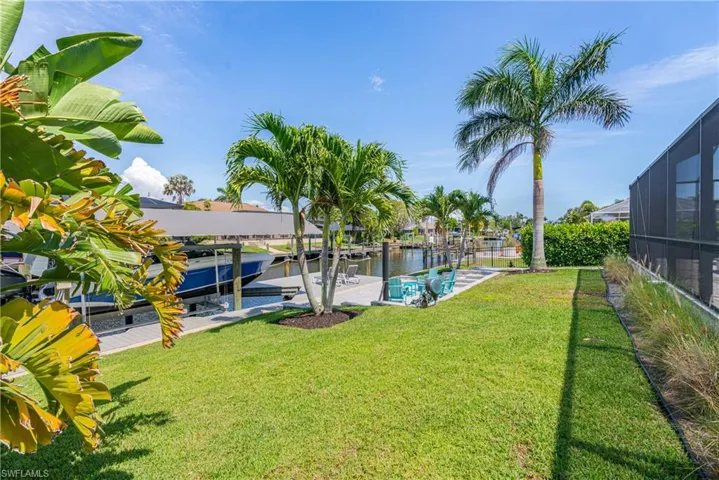 View of grassy yard with boat lift, a dock, a lanai, and a water view