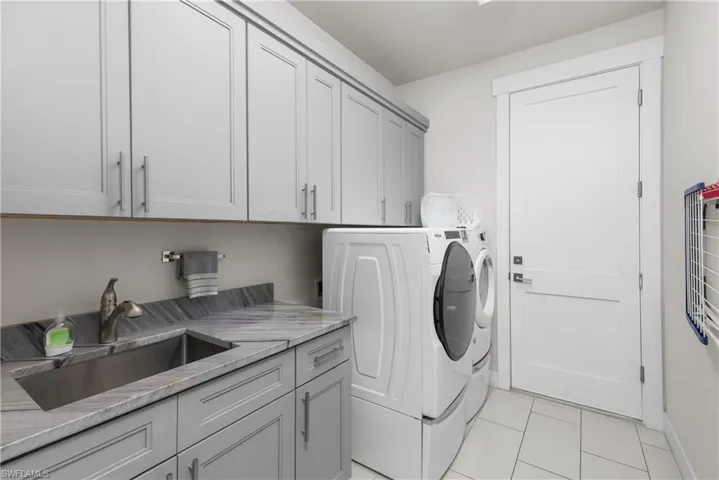 Laundry area featuring cabinet space, washing machine and clothes dryer, light tile patterned floors, and baseboards