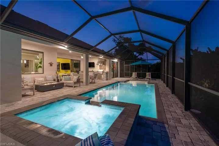 View of pool with a patio, an outdoor kitchen, an outdoor living space with a fire pit, a pool with connected hot tub, and glass enclosure