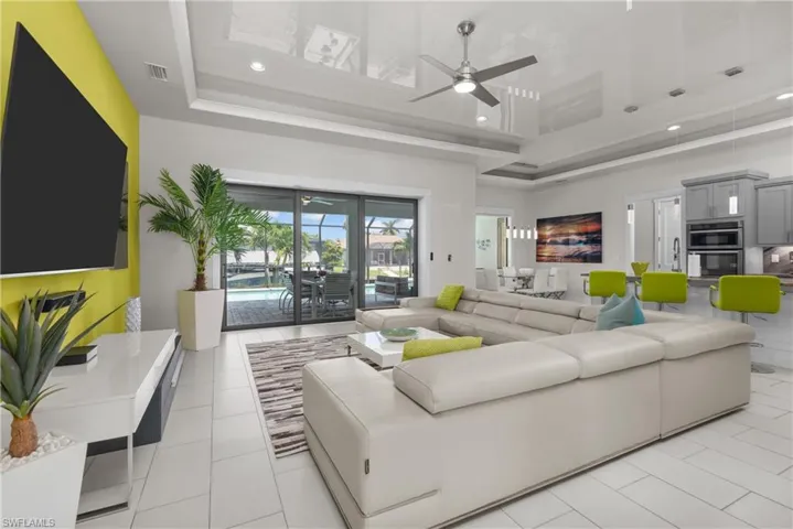 Living room with ceiling fan, recessed lighting, a high ceiling, a tray ceiling, and light tile patterned flooring