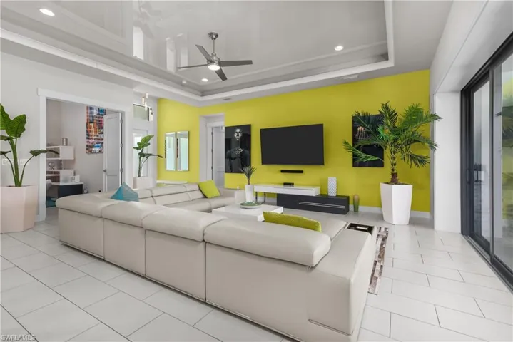 Tiled living room with a ceiling fan, recessed lighting, a tray ceiling, baseboards, and a high ceiling