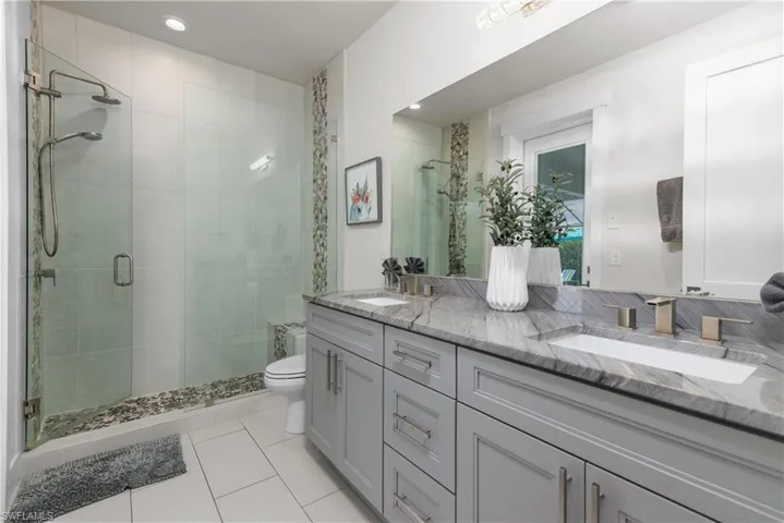 Full bath with double vanity, a shower stall, toilet, tile patterned flooring, and recessed lighting