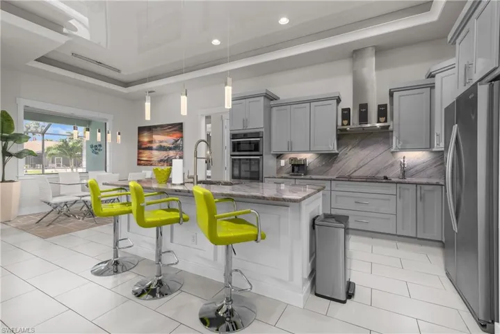 Kitchen with stainless steel appliances, gray cabinets, island exhaust hood, dark stone counters, and a breakfast bar area
