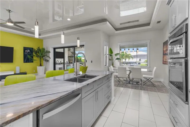 Kitchen with a sink, stainless steel dishwasher, a raised ceiling, light stone countertops, and decorative light fixtures