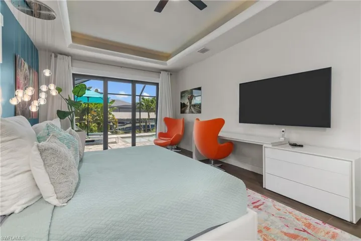 Bedroom with a raised ceiling, access to exterior, wood finished floors, and a ceiling fan