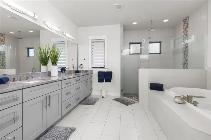 Full bath with a stall shower, double vanity, tile patterned flooring, a bath, and baseboards