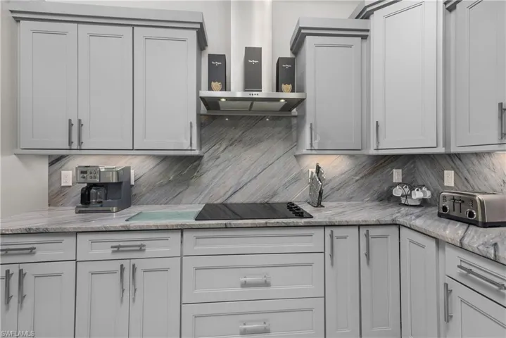 Kitchen featuring wall chimney exhaust hood, black electric stovetop, tasteful backsplash, and light stone counters
