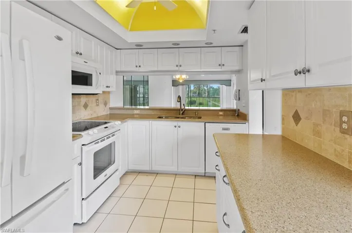 Kitchen featuring white appliances, backsplash, sink, ceiling fan, and white cabinets