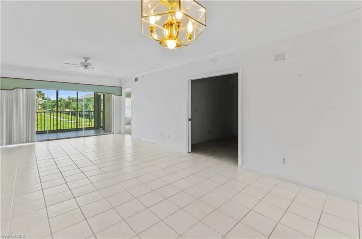 Tiled empty room featuring ceiling fan with notable chandelier and ornamental molding