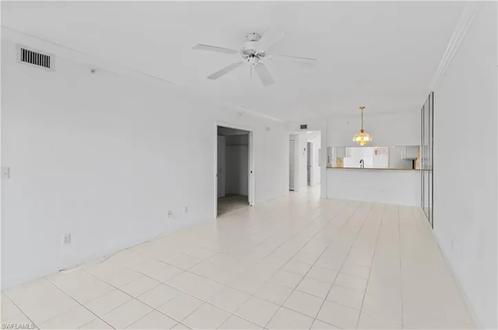 Unfurnished living room with ceiling fan with notable chandelier, light tile patterned floors, and crown molding