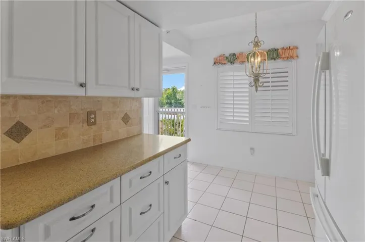 Kitchen with a notable chandelier, white fridge, white cabinetry, backsplash, and hanging light fixtures