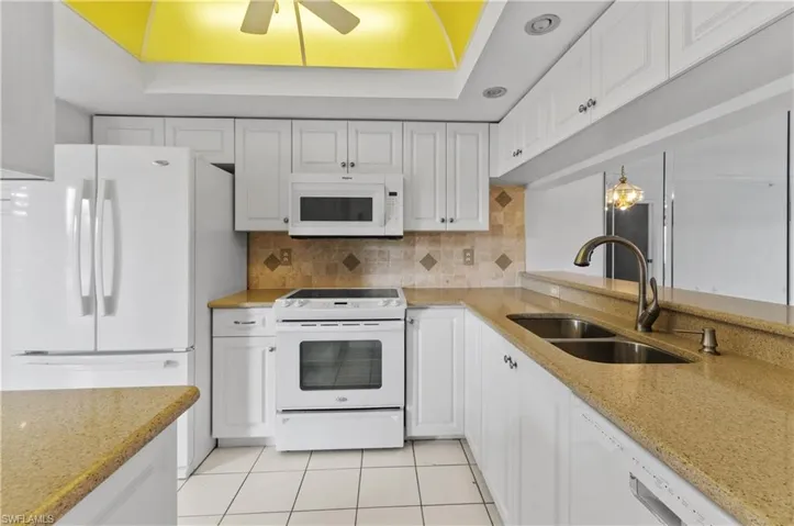Kitchen featuring ceiling fan, sink, white appliances, and a tray ceiling