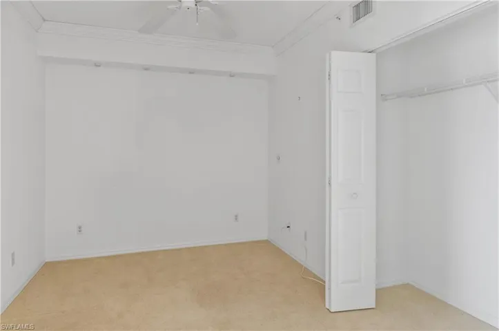 Unfurnished bedroom featuring crown molding, ceiling fan, a closet, and light colored carpet