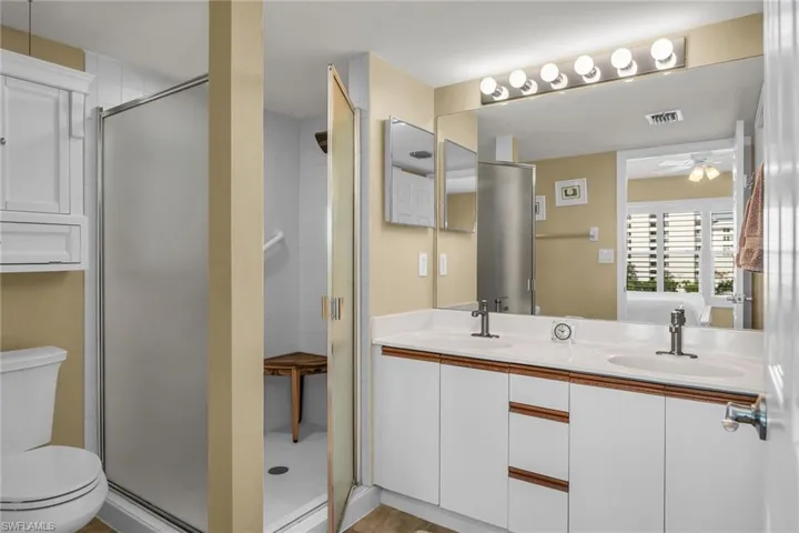 Bathroom featuring toilet, double vanity, a ceiling fan, and a stall shower