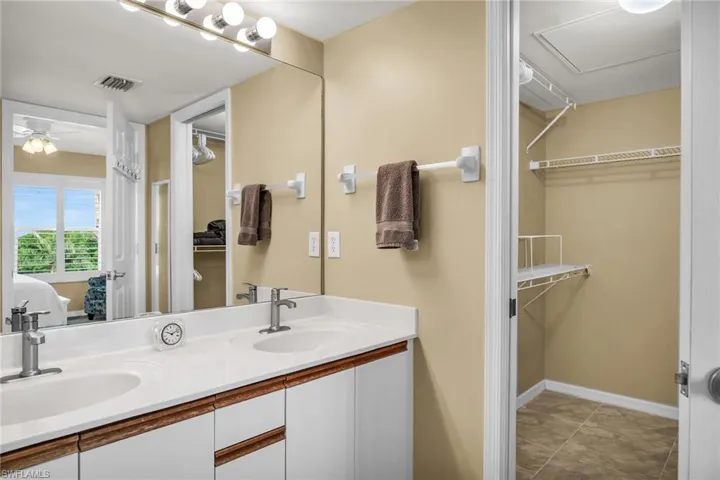 Ensuite bathroom featuring double vanity, a walk in closet, a ceiling fan, and baseboards