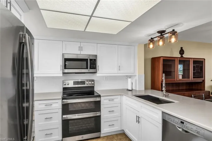 Kitchen with appliances with stainless steel finishes, a sink, white cabinetry, and light countertops