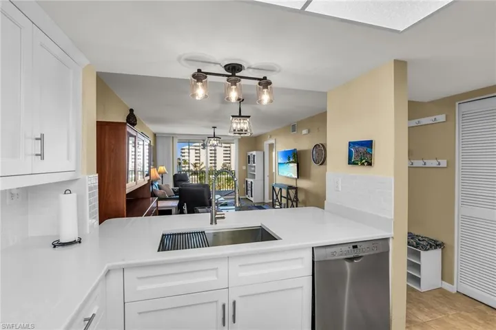 Kitchen featuring stainless steel dishwasher, backsplash, light countertops, a sink, and white cabinetry