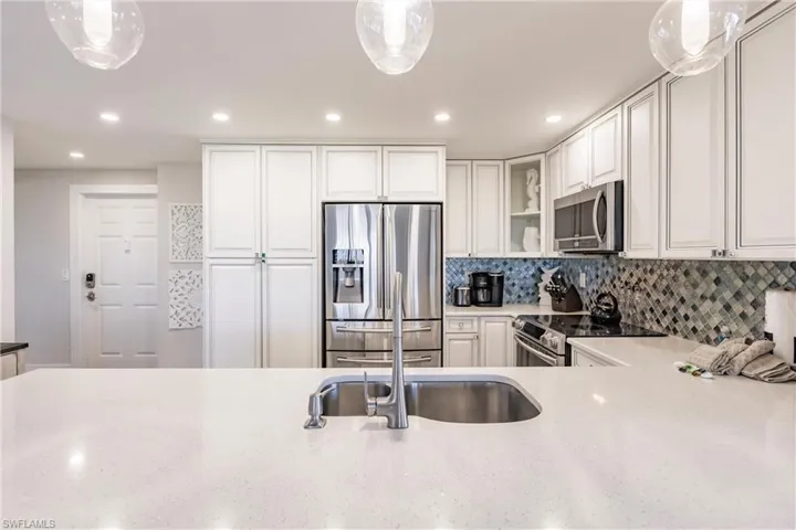 Kitchen with decorative light fixtures, decorative backsplash, white cabinetry, and stainless steel appliances