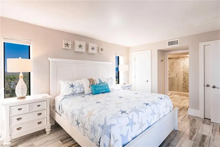 Bedroom with ensuite bath, light hardwood / wood-style floors, and multiple windows