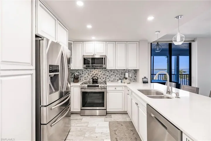 Kitchen with sink, hanging light fixtures, tasteful backsplash, white cabinets, and appliances with stainless steel finishes