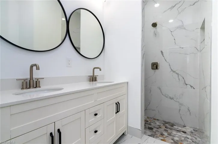Full bath featuring double vanity, marble finish floor, a sink, and a marble finish shower