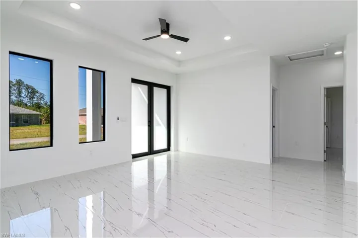 Empty room with a raised ceiling, attic access, and a healthy amount of sunlight