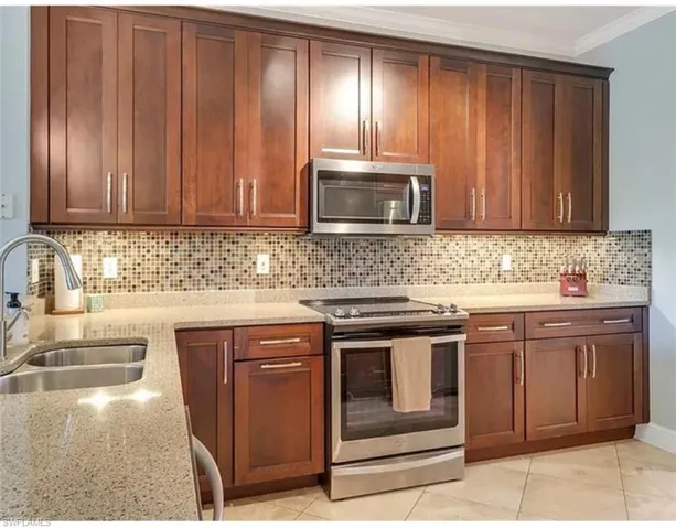 Kitchen with appliances with stainless steel finishes, a sink, ornamental molding, light stone countertops, and tasteful backsplash