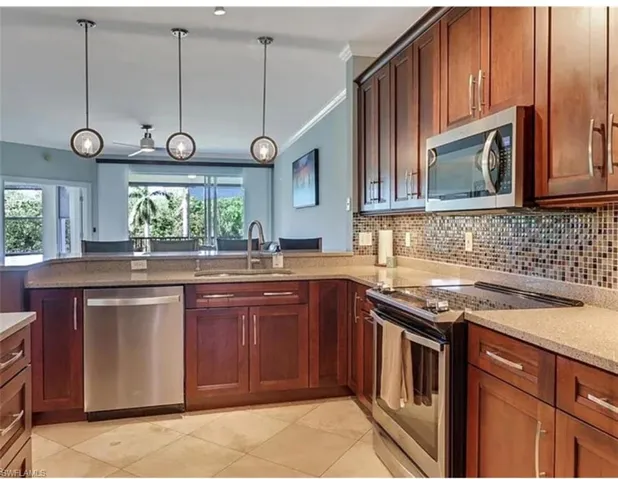 Kitchen featuring appliances with stainless steel finishes, a sink, light tile patterned floors, light stone countertops, and tasteful backsplash