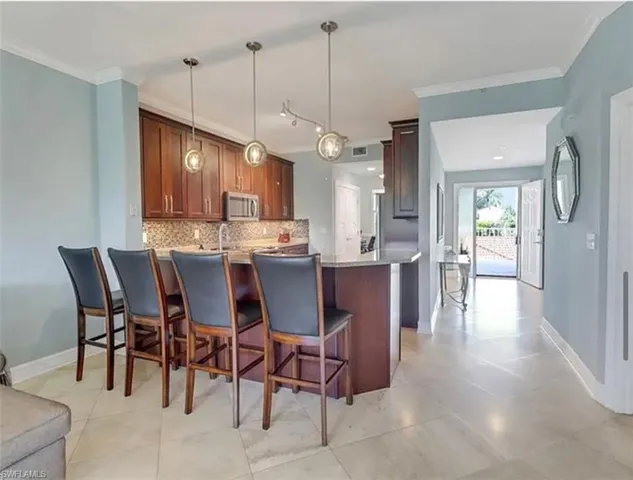Kitchen with stainless steel microwave, a peninsula, backsplash, ornamental molding, and a breakfast bar area