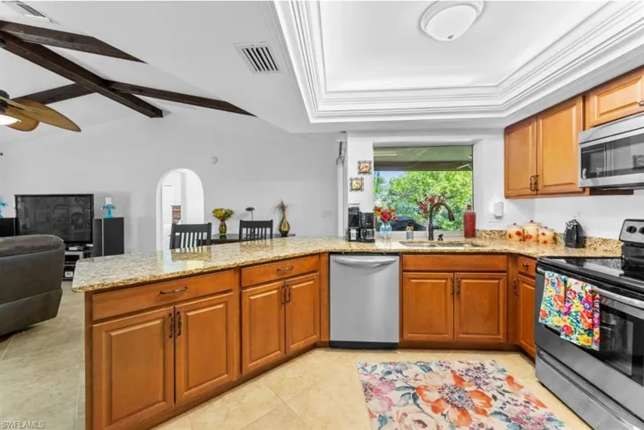Kitchen with appliances with stainless steel finishes, brown cabinets, light stone counters, a peninsula, and open floor plan