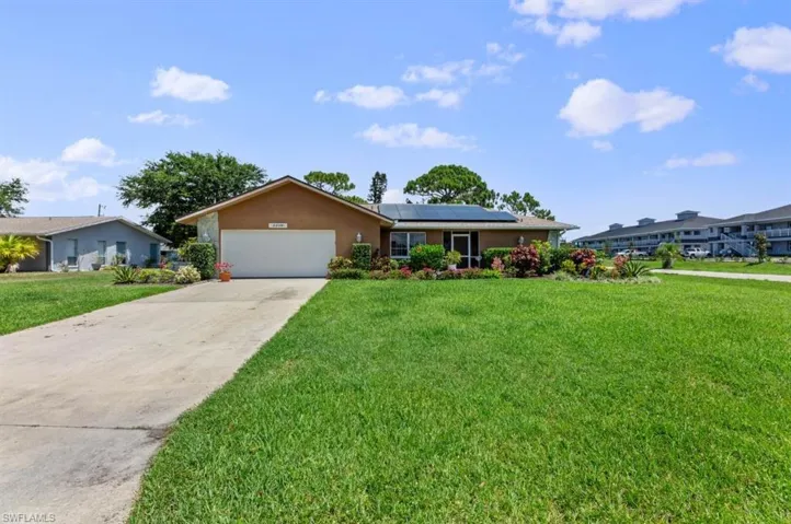Single story home with roof mounted solar panels, concrete driveway, a front yard, stucco siding, and a garage
