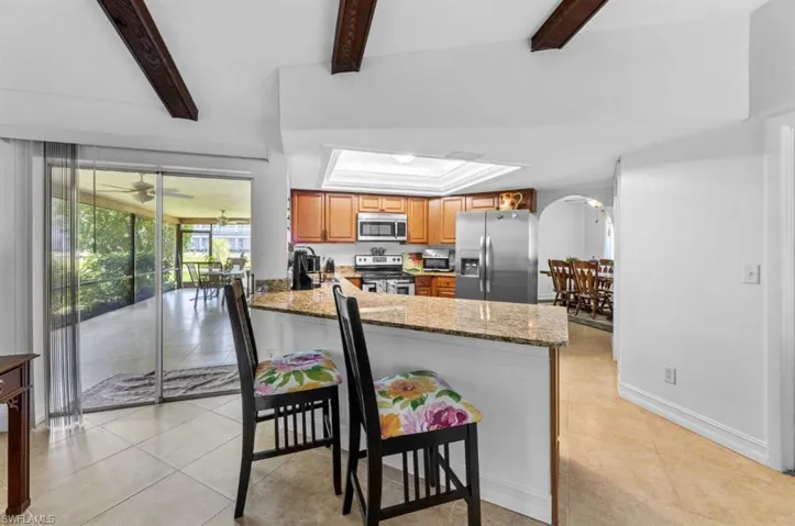 Kitchen featuring appliances with stainless steel finishes, dark stone countertops, brown cabinetry, arched walkways, and light tile patterned flooring