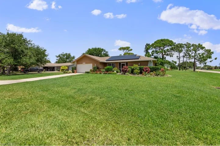 Ranch-style home featuring a front yard, concrete driveway, roof mounted solar panels, a garage, and stucco siding