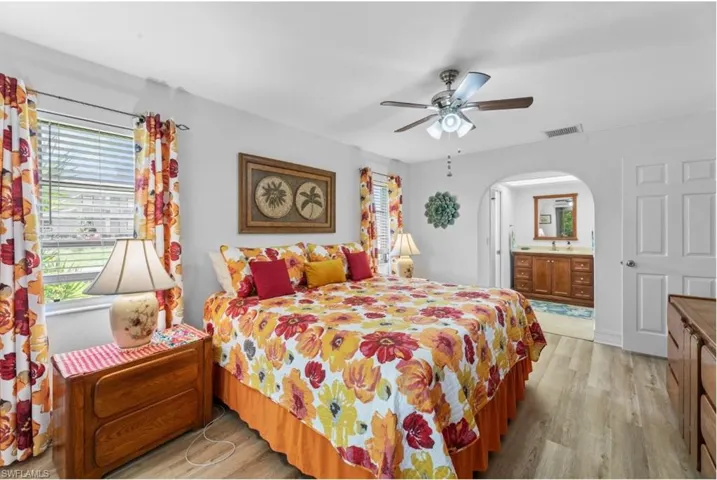 Bedroom with light wood-style flooring, a ceiling fan, multiple windows, and arched walkways