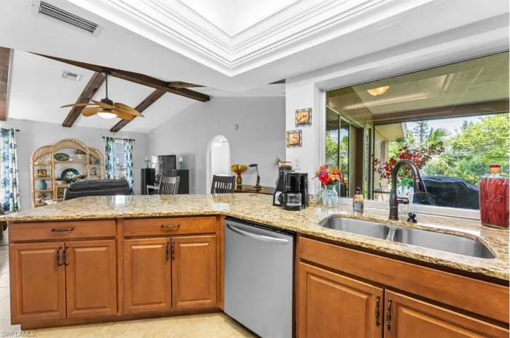 Kitchen with stainless steel dishwasher, brown cabinetry, light stone counters, and open floor plan