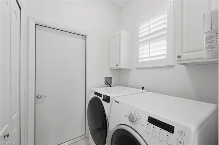 The well-appointed laundry room offers exceptional functionality with a spacious storage closet, additional cabinetry above the washer and dryer for added organization, and a window that fills the space with natural light.