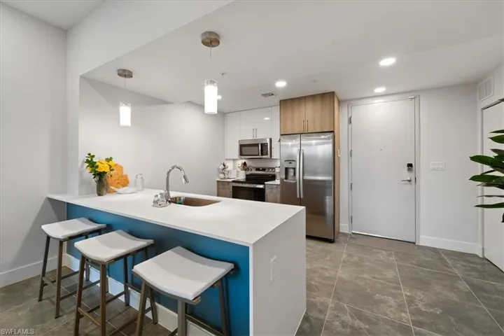 Kitchen featuring stainless steel appliances, light countertops, white cabinetry, pendant lighting, and a sink