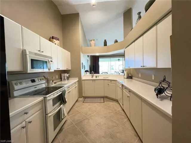 Kitchen featuring white appliances, light countertops, high vaulted ceiling, white cabinets, and light tile patterned floors