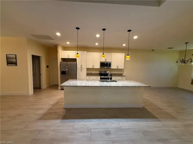 Open-concept kitchen featuring an oversized island with granite countertop, stainless steel appliances, pendant lighting, and recessed lighting