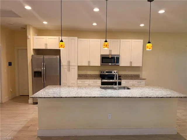 Spacious kitchen featuring a large island with an undermount sink, granite countertops, white shaker cabinetry, stainless steel appliances, and recessed lighting